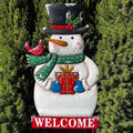 The Snowman Welcome Garden Stake by Available for Pick-Up & Delivery features a cheerful snowman in a top hat and green scarf holding a gift, with a red cardinal perched on its arm. This charming garden stake adds holiday allure, standing among greenery with a WELCOME sign beneath.
