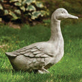 The All Delivery Options Statue – Cast Stone – Duck features detailed feathers and a raised head, creating a charming accent on green grass with softly blurred leafy plants in the background.