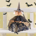 The Witch - Naomi - 23 doll by Available for Pick-Up & Delivery showcases a hand-painted face, a plaid pointed hat, and a black dress with gold patterns. Shes seated on a white bench holding her broom beneath black bat wall decorations.